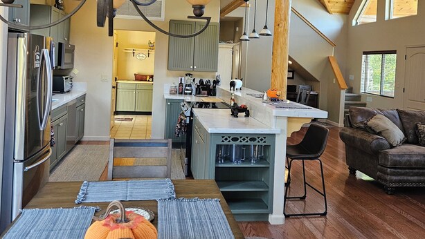 Una cocina amplia con una isla central, vigas de madera en el techo y un comedor con mesa dispuesta para cuatro.