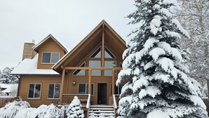 Una cabaña de madera con un amplio porche, múltiples ventanas y un paisaje cubierto de nieve.