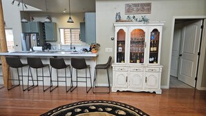 Una cocina con taburetes de bar, un armario blanco con puertas de cristal y techo de madera.