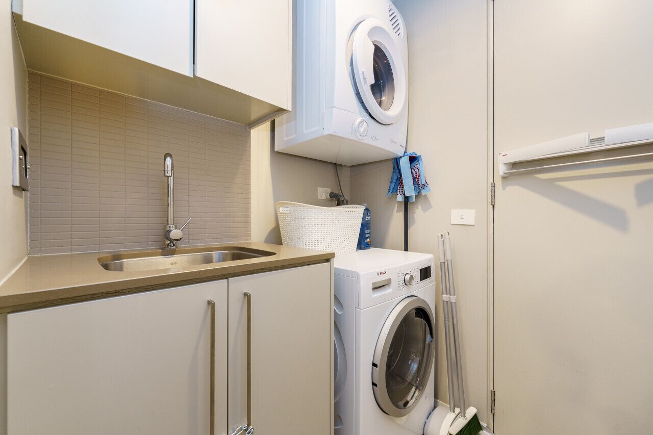 A compact laundry room with a washing machine, a sink, and a drying rack.