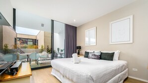 Een moderne hotelkamer met een groot bed, een bureau en een glazen wand met uitzicht op het terras.