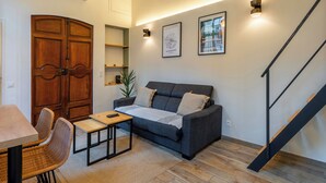 A cozy living room with a sofa, a small table, and a chair. There is a wooden cabinet and a staircase in the background.