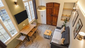 A spacious living area with a wooden dining table, a sofa, and a TV mounted on the wall.