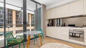 A modern kitchen with a large window, a dining area with green chairs, and a view of the cityscape.