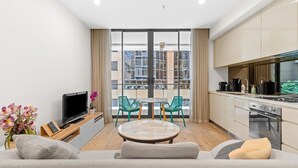 A modern living room with a sofa, a TV, a small table, and a balcony with a view of buildings.