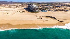 An aerial view of a coastal area with a large building, sandy beach, and clear blue waters.