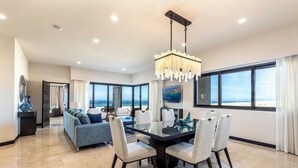 A spacious living area with a large dining table, comfortable seating, and a view of the ocean through large windows.