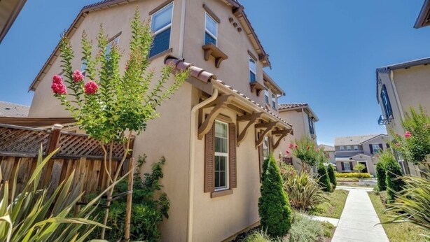 A two-story house with a beige exterior, a wooden deck, and a garden with various plants and flowers.
