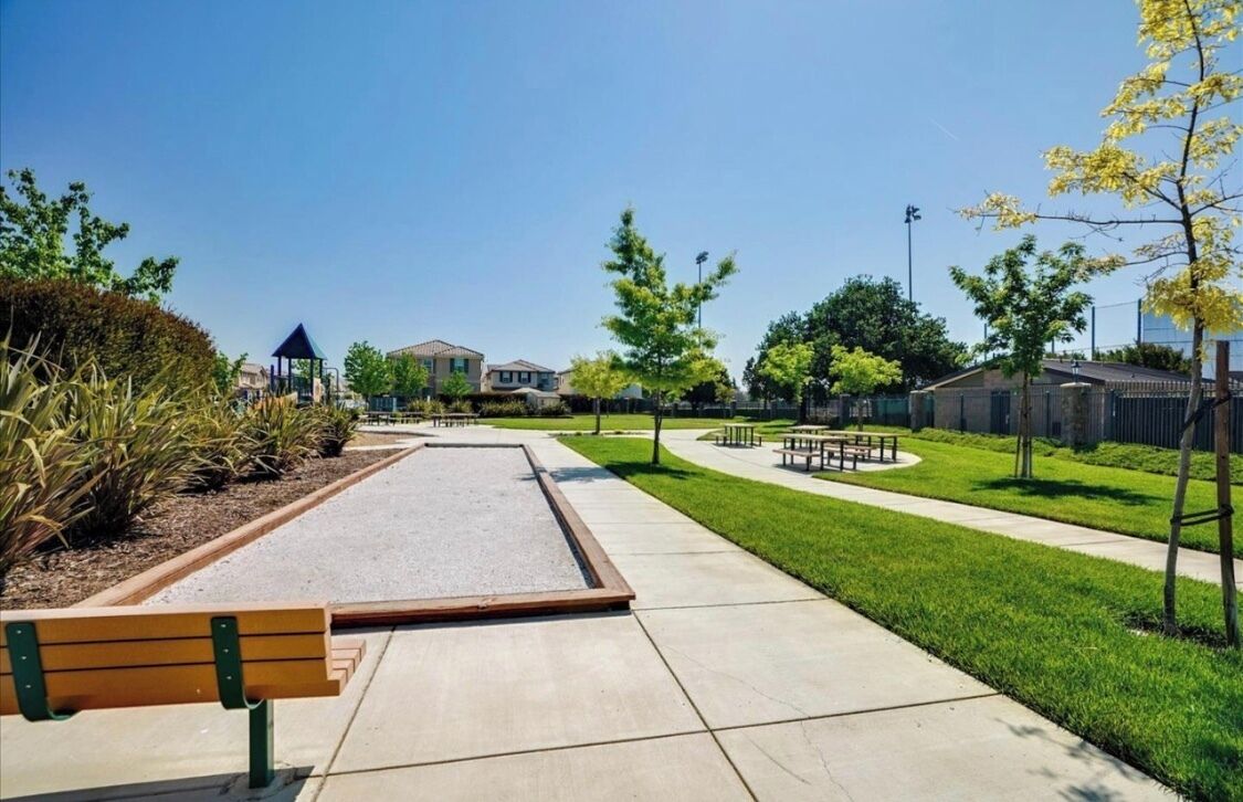 A park with a paved walkway, benches, and a playground area.