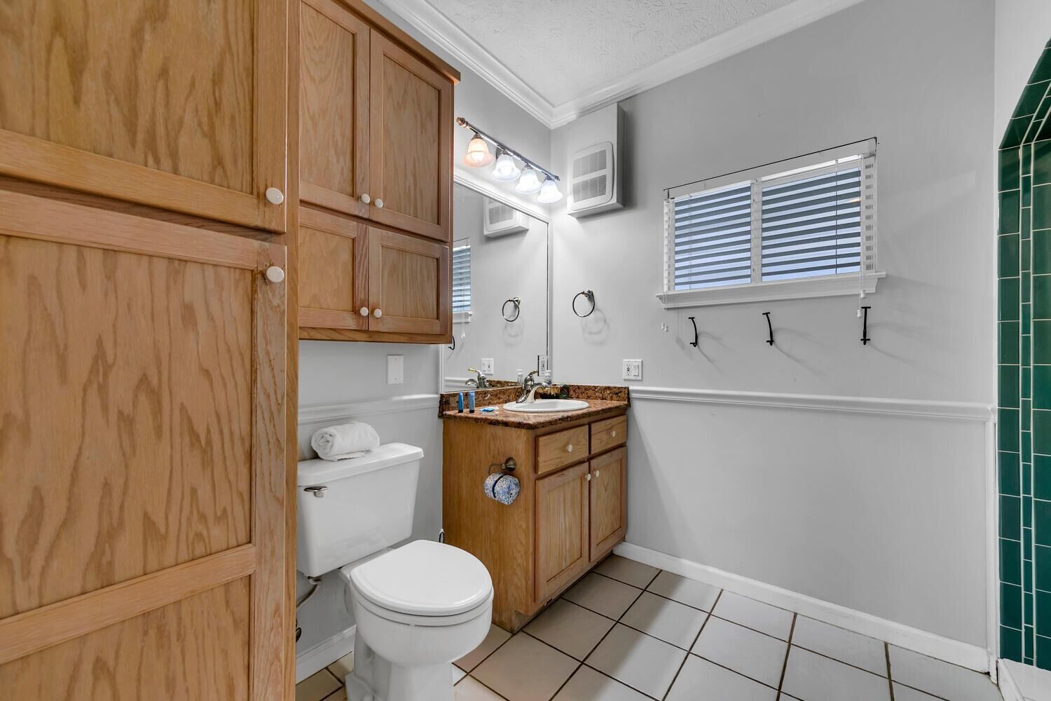A bathroom with wooden cabinets, a white toilet, a sink with a countertop, and a window with blinds.