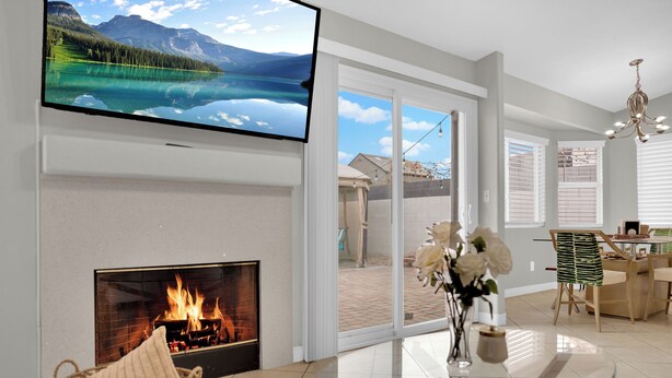 A modern living room with a fireplace, a glass table, and a TV displaying a scenic landscape. - Henderson escape+ mini golf +peaceful stay (Henderson)