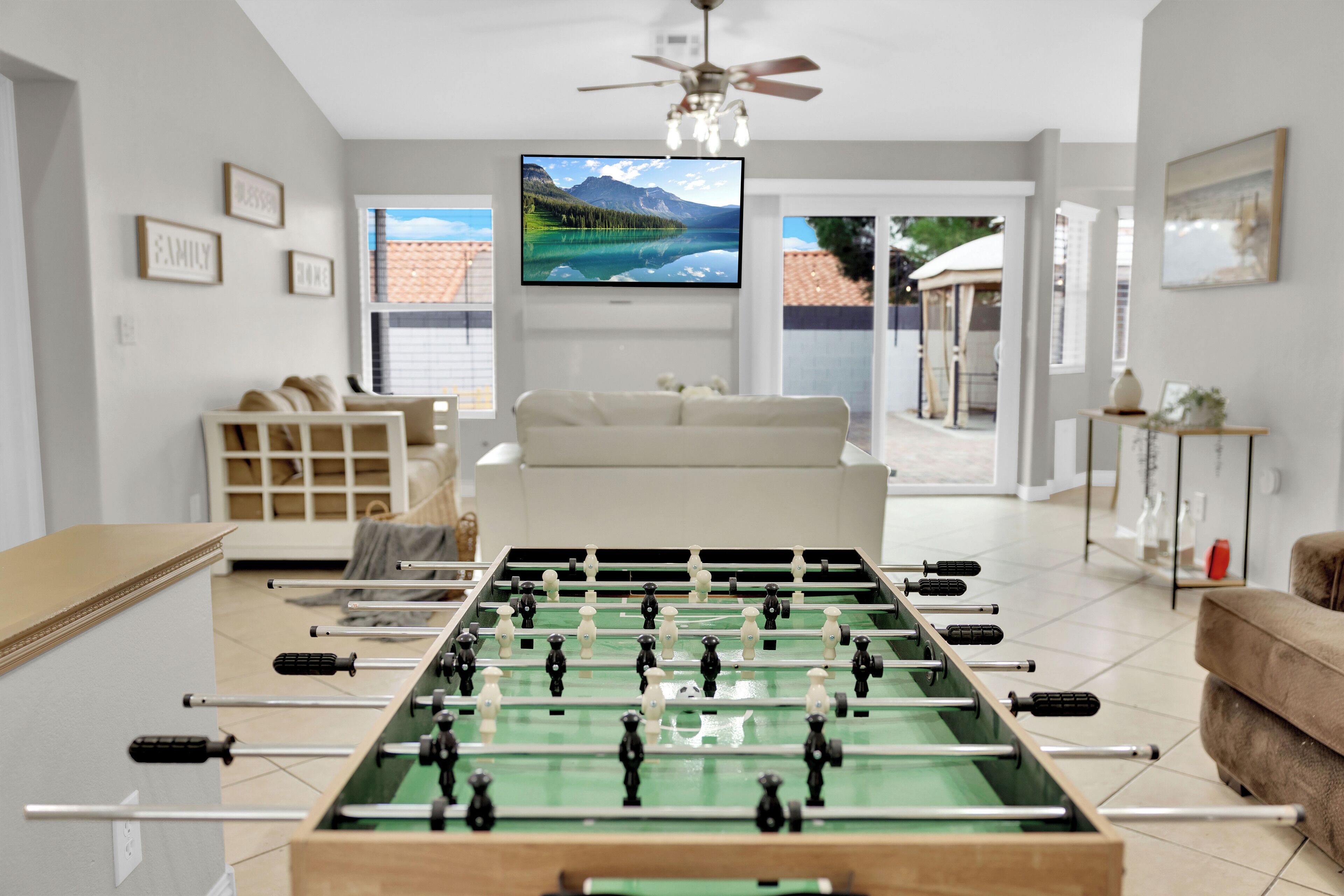 Una sala de estar con una mesa de fútbol de mesa, un televisor montado en la pared y un sofá.