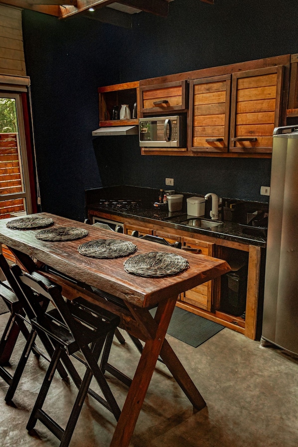Une cuisine avec des meubles en bois, un réfrigérateur en acier inoxydable et une longue table en bois surmontée de sets de table en fibres tressées.