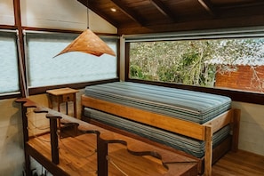 A room with a wooden bench, a hanging light fixture, and a large window with a view of greenery outside.
