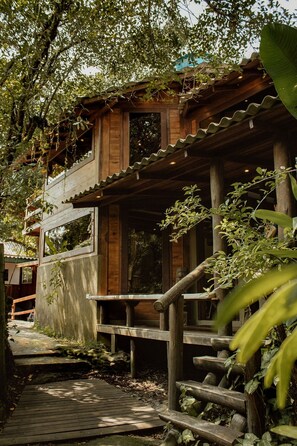 A wooden cabin with a wooden staircase leading to a deck, surrounded by lush greenery. - Surfway Ilha do Mel (Paranaguá)