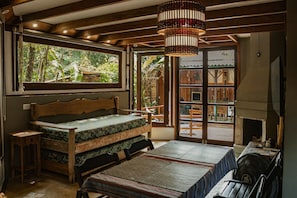 Une pièce avec un lit, une table et une cheminée. Il y a une fenêtre qui donne sur un paysage verdoyant.