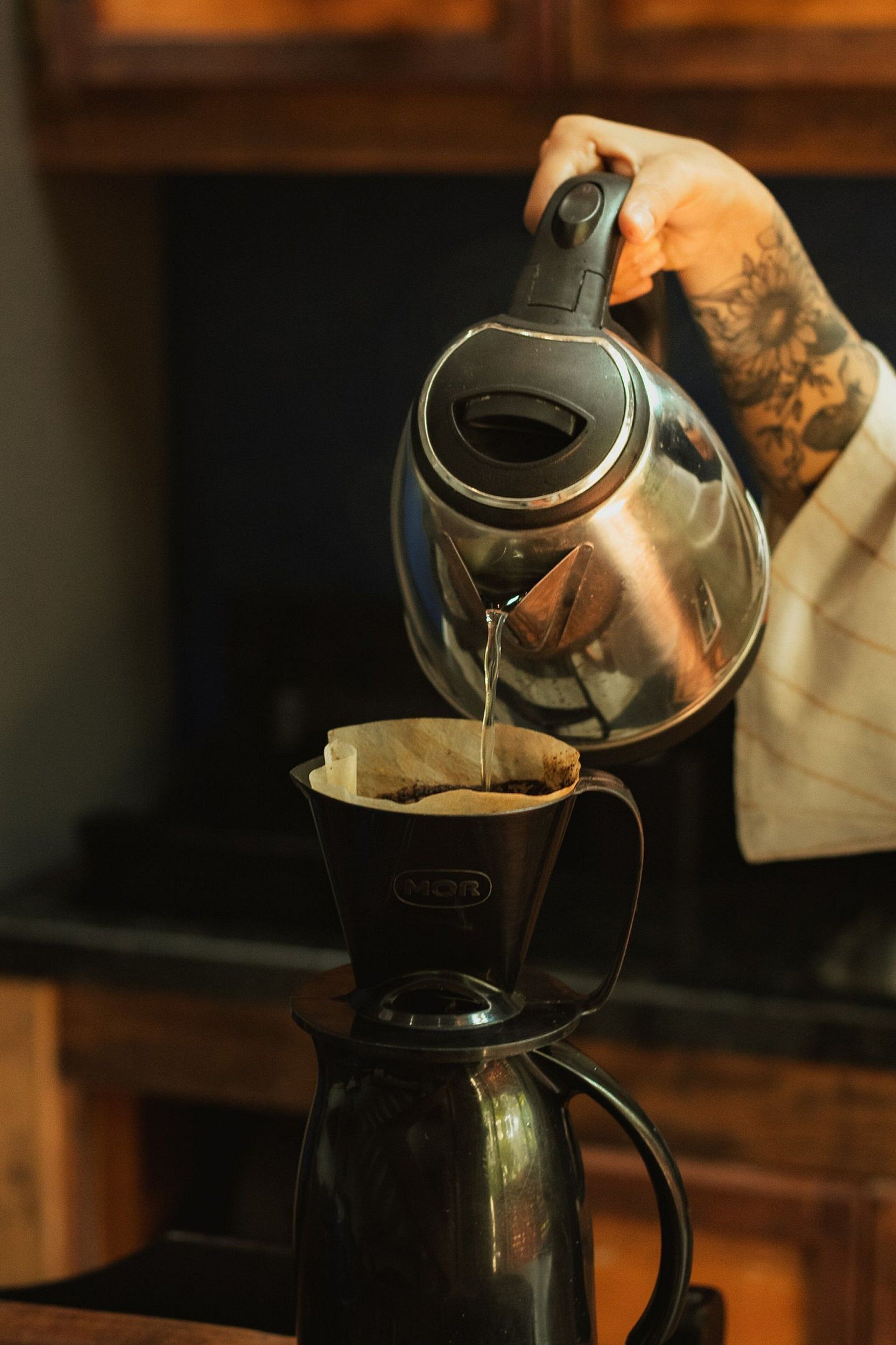 A person pouring liquid from a kettle into a coffee maker.