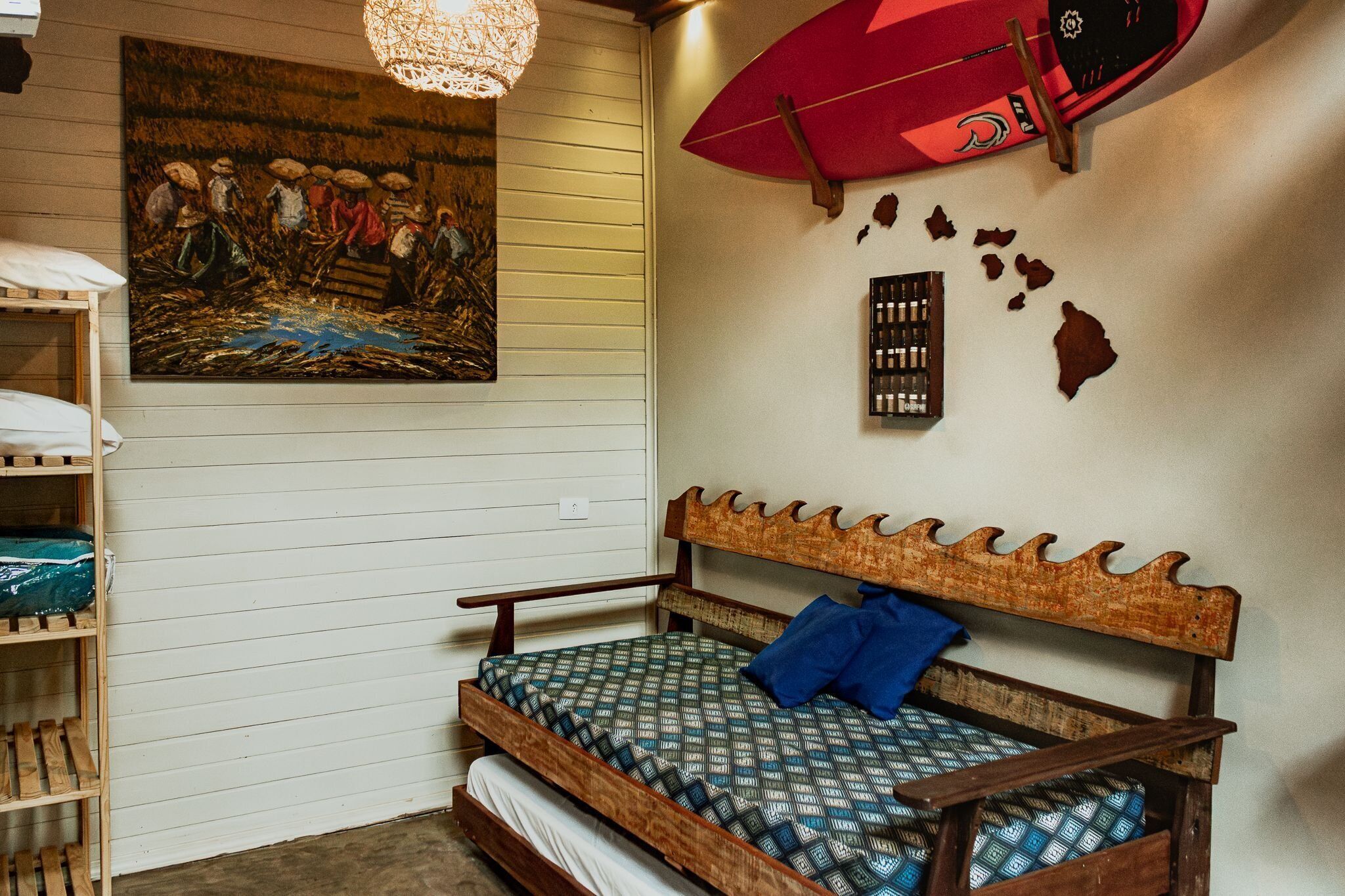 A room with a wooden bed, a wall-mounted surfboard, a painting, and a shelf with folded blankets.