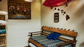 A room with a wooden bed, a wall-mounted surfboard, a painting, and a shelf with folded blankets.
