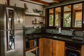 A kitchen with stainless steel appliances, wooden cabinets, a black countertop, and a window with a view of greenery.