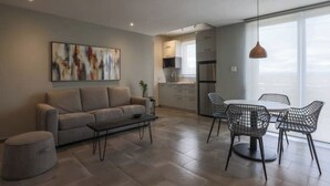 A modern living room with a sofa, coffee table, and wireframe chairs. A kitchen is visible in the background with a dining table and chairs. - Old San Juan Guesthouse.Free Parking, Rooftop & Generator – Casa Terra Porto #8 (San Juan)