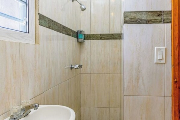 Un baño con lavamanos, ducha y una pared de acento de madera.