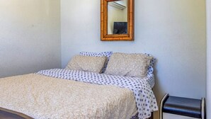 A bedroom with a bed, pillows, a patterned bedspread, a wooden headboard, a small bedside table, and a mirror on the wall. - Beach House Walk To The Beach #2

 (San Juan)