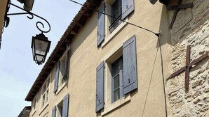 A building with a stone facade, multiple windows with shutters, and a large wooden door. - Maison Cosy Lodge, 15 p, clim, wifi, cour, garage (Montfrin)