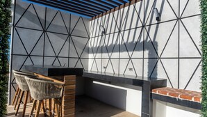 Eine Außenküche mit integriertem Grill, Sitzgelegenheiten und einer geometrischen Wandgestaltung.