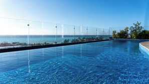 A clear blue infinity pool with a glass barrier, overlooking a coastal view. - Menesse Apartment  (Playa del Carmen)