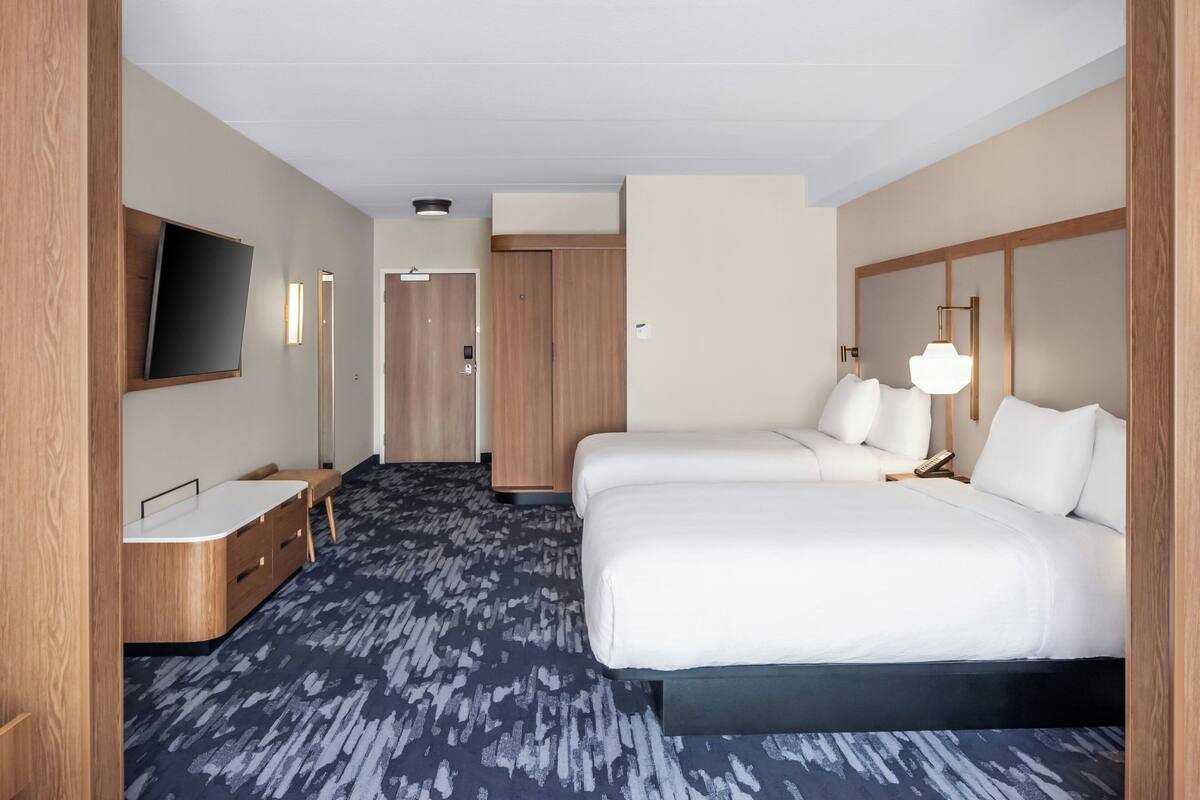 A hotel room with a bed, bedside table, lamp, and a TV mounted on the wall.