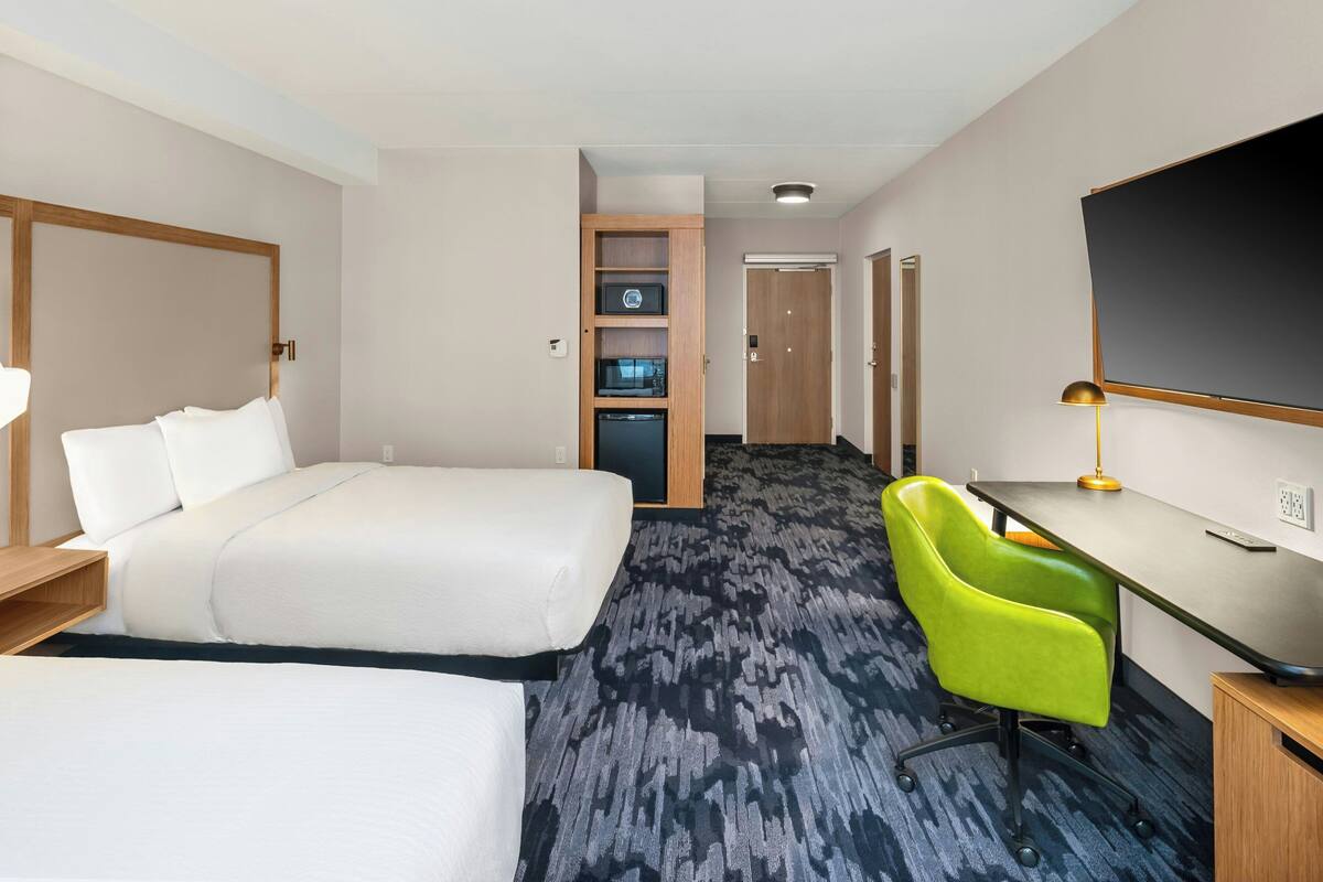 A hotel room with a bed, a desk, a chair, a TV, and a minibar.