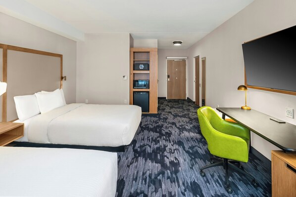 A hotel room with a bed, a desk, a chair, a TV, and a minibar.