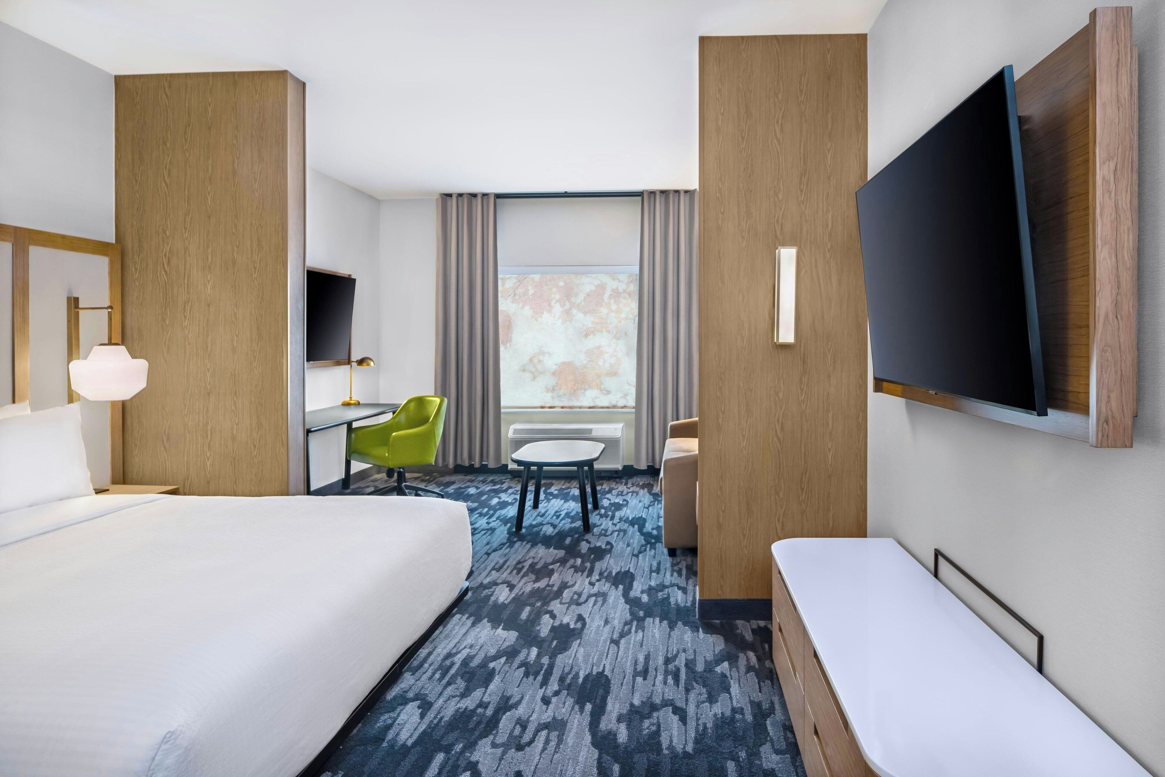 A hotel room with a large bed, a desk, a chair, a TV, and a view of the outdoors.