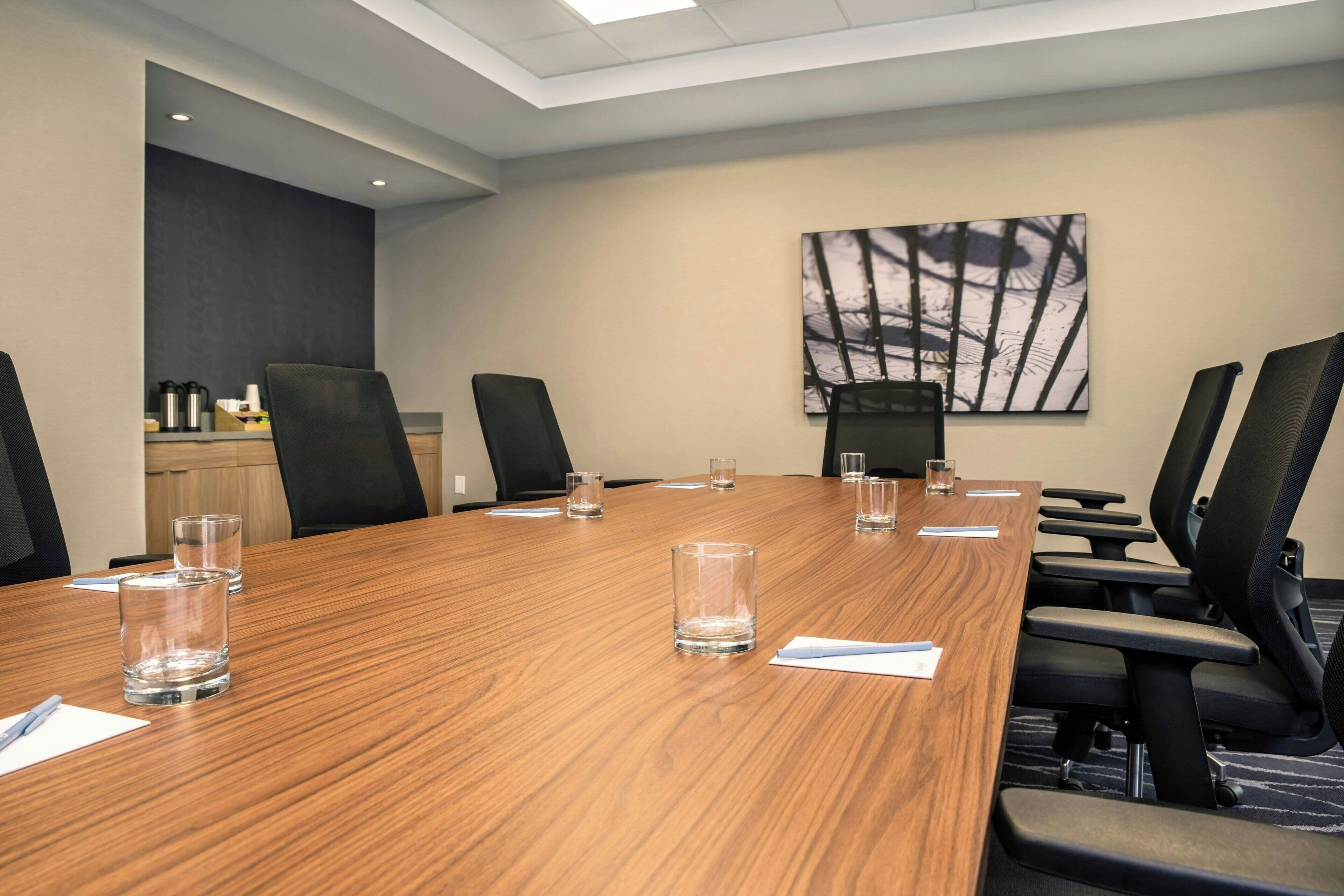 A conference room with a long wooden table, black chairs, and a painting on the wall.