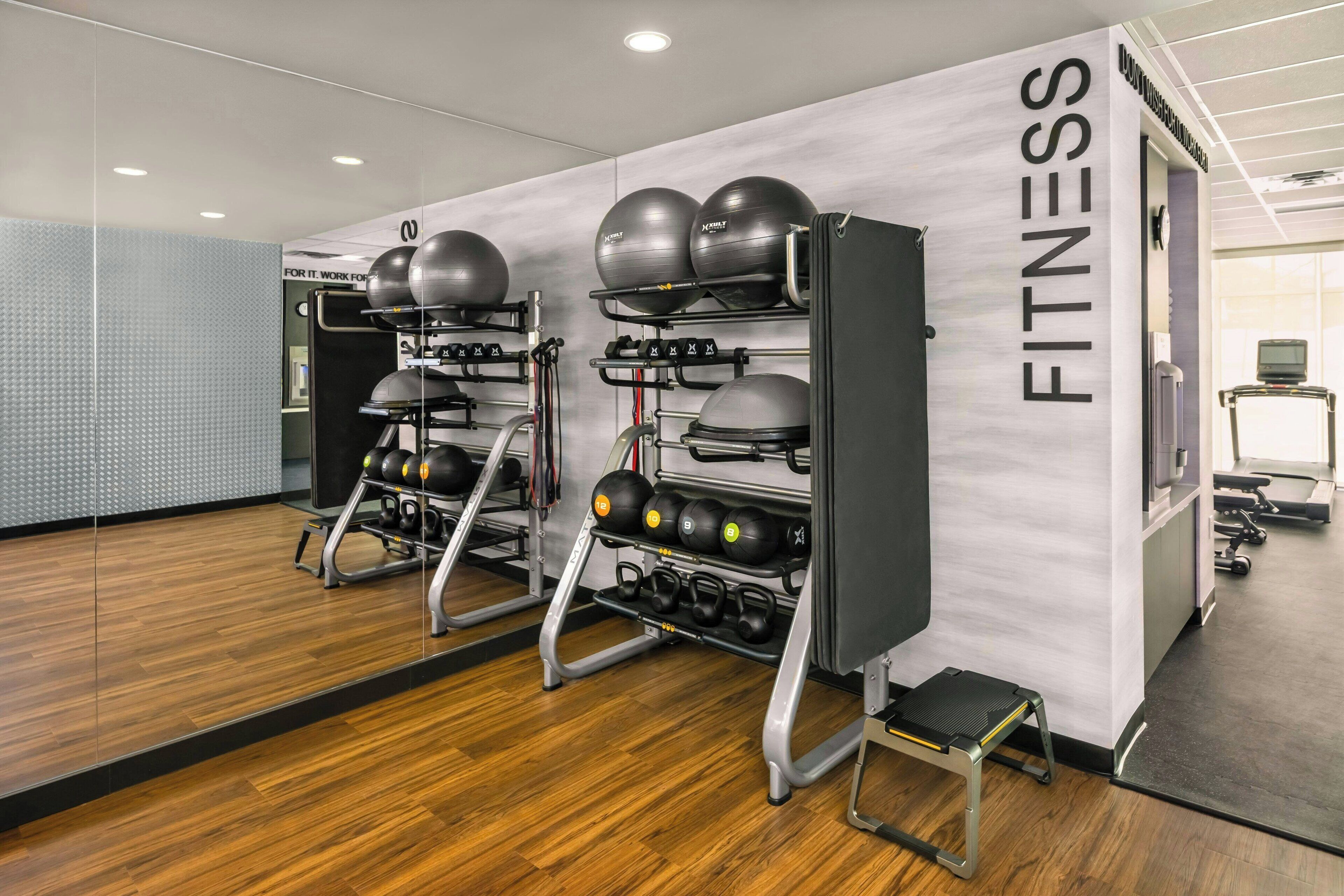 Une salle de sport équipée de matériel d’exercice, dotée d’un mur recouvert de miroirs et d’une enseigne indiquant « FITNESS ».