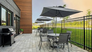 Eine Terrasse im Freien mit Tischen, Stühlen, Sonnenschirmen und einem Grill.