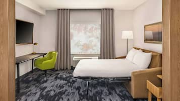 Una habitación de hotel con una cama, un escritorio, una silla verde, una lámpara y una ventana con cortinas.