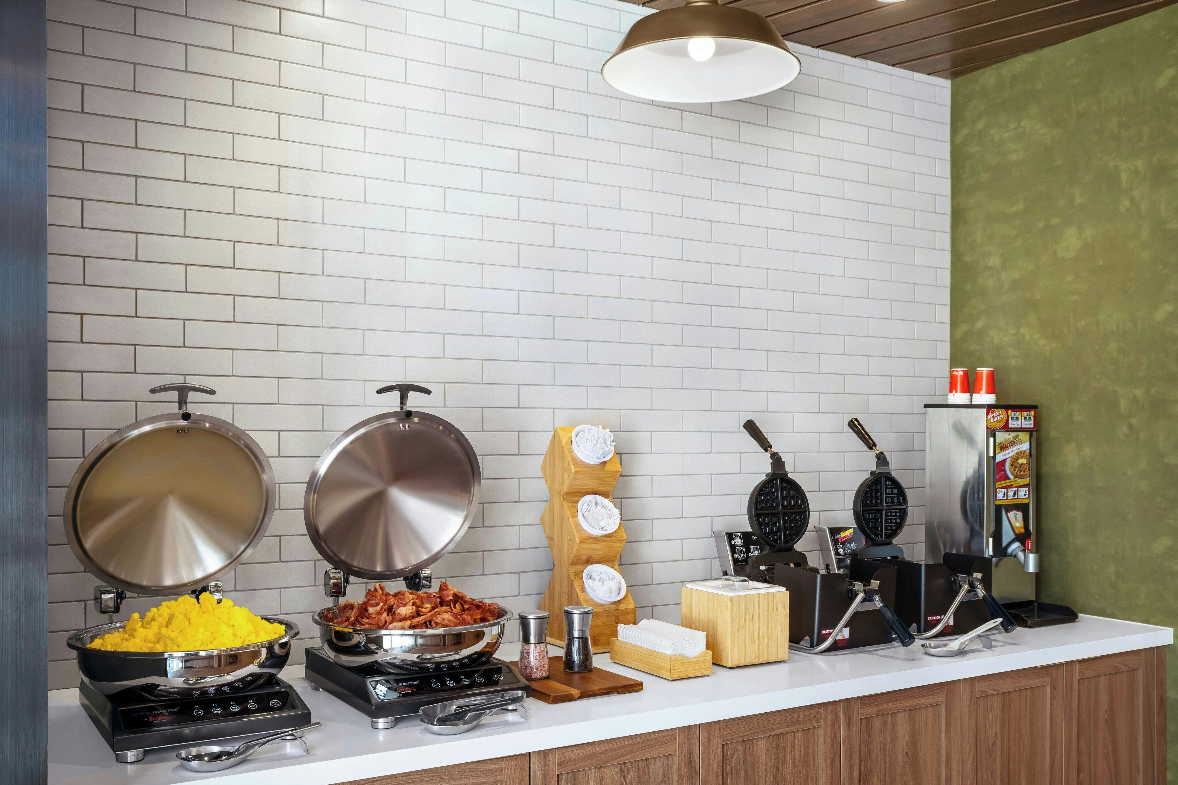 A buffet setup with various food stations including a waffle maker, a rice cooker, and a griddle.