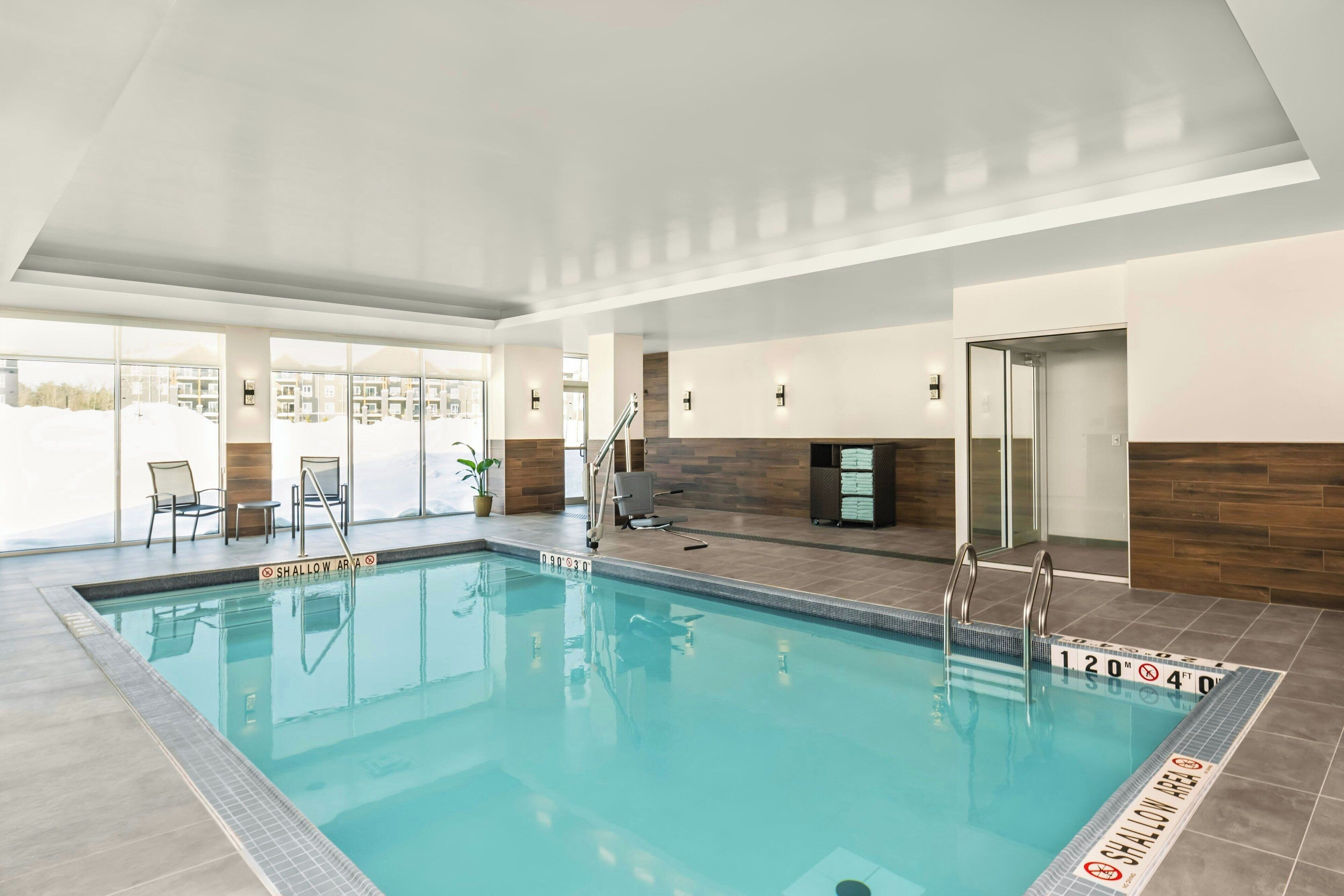 Une piscine intérieure avec des lignes de démarcation bien visibles pour les couloirs, un panneau indiquant la zone peu profonde et une vue sur l’extérieur.
