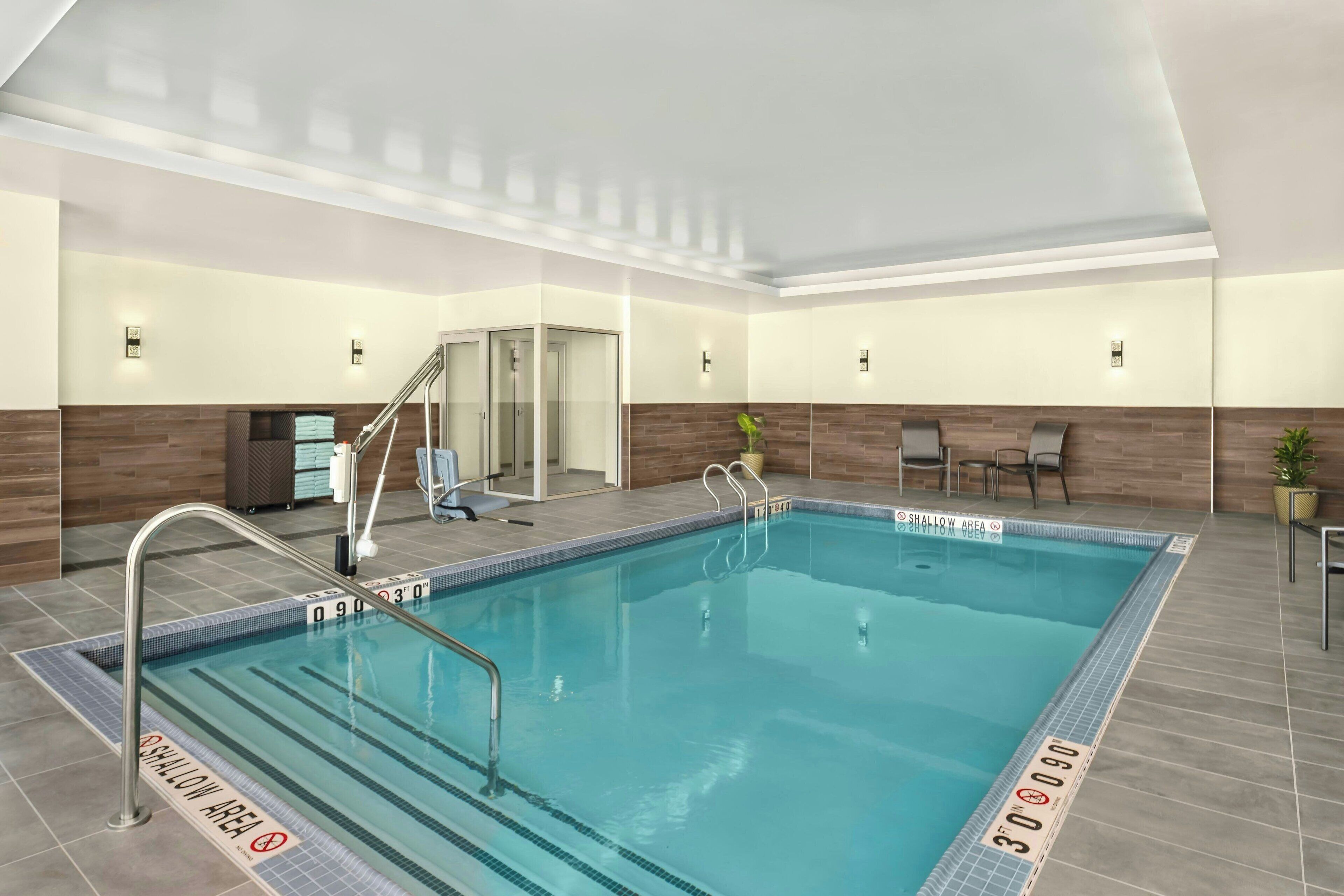 An indoor swimming pool with clear lane markings, a shallow area sign, and a glass door entrance.