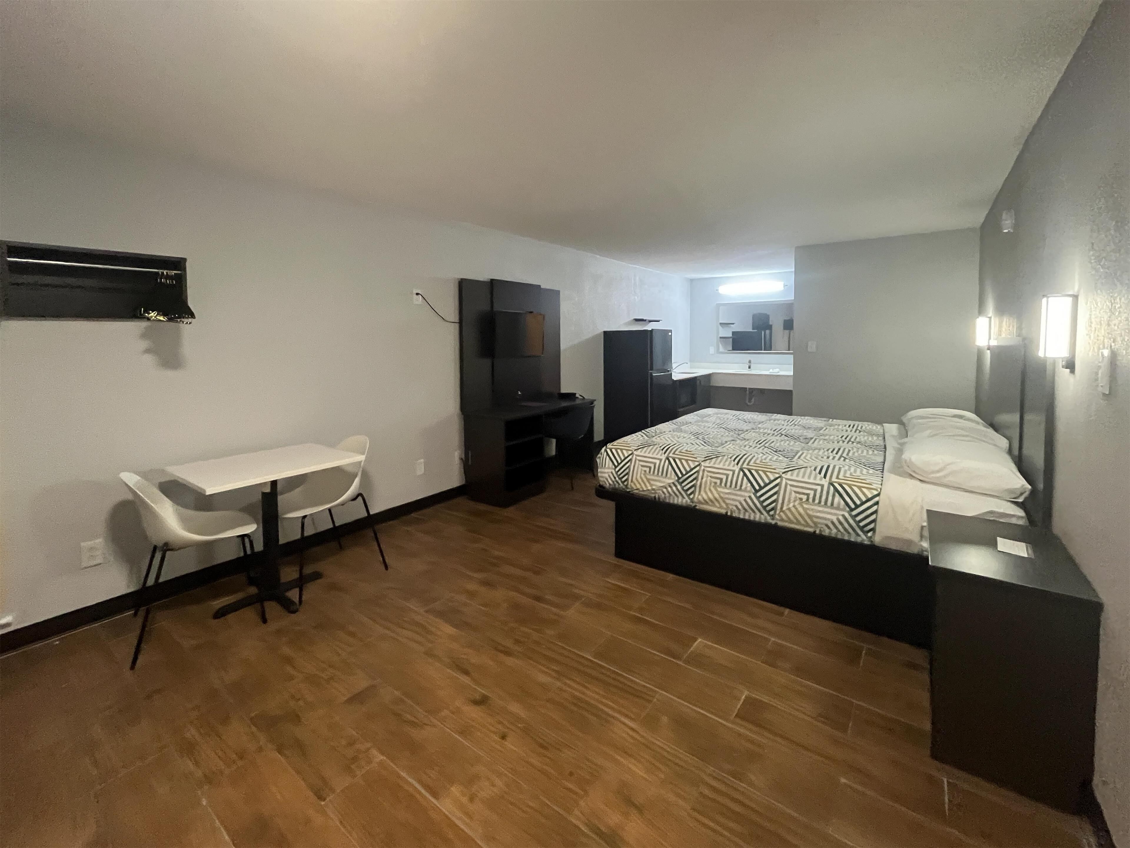 Een compacte hotelkamer met een eenpersoonsbed, een klein bureau met stoel, een televisie en een kitchenette.