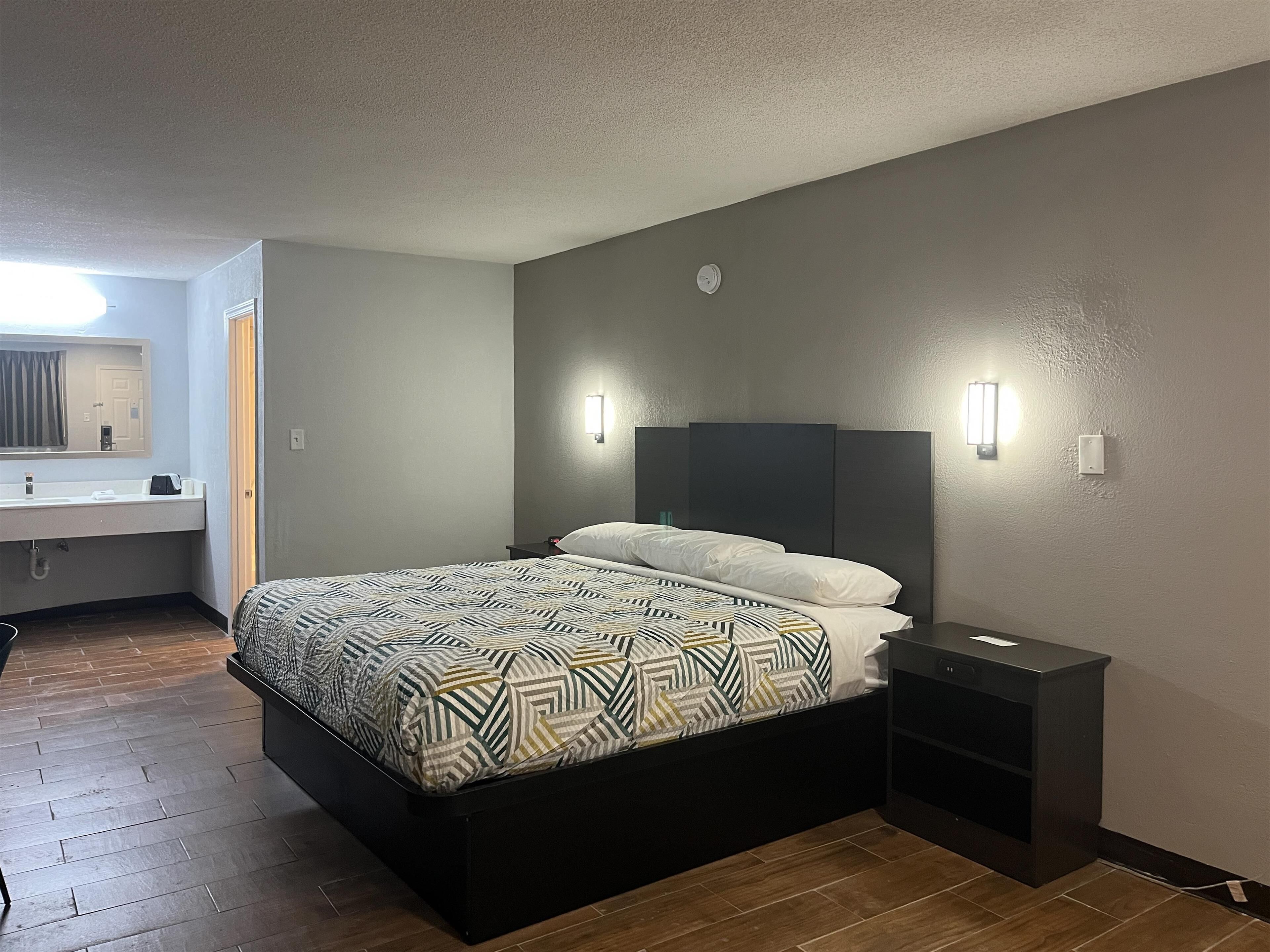 Une chambre d’hôtel moderne avec un grand lit, une table de chevet, une petite table et une étagère intégrée.