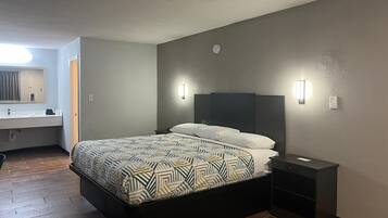 Une chambre d’hôtel moderne avec un grand lit, une table de chevet, une petite table et une étagère intégrée.