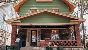 Une maison à deux étages, avec une façade verte, des fondations en briques et un porche à l’avant où est affiché le numéro « 4235 ».