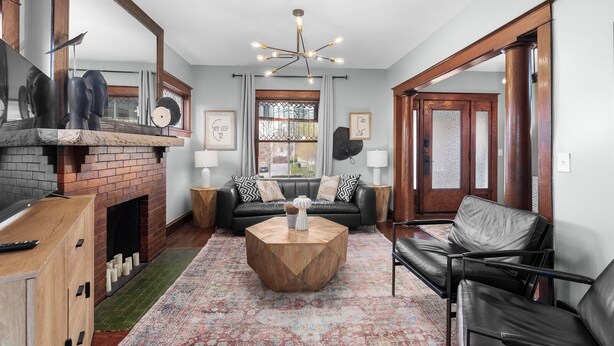 Un salon avec une cheminée, un canapé en cuir noir, une table basse en bois et un tapis à motifs.