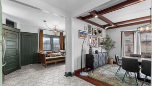 Un salon moderne avec un canapé, une table à manger et des chaises. On y trouve une fenêtre avec des rideaux, un lustre et un mur décoré d’un motif.
