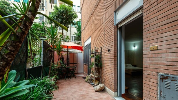 A narrow brick pathway leading to a room with a bed, a small table, and chairs.