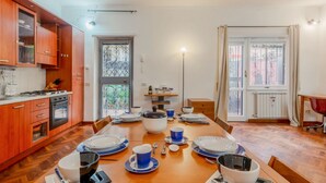 A dining area with a wooden table set for four, kitchen cabinets, a stove, and a view through a window.