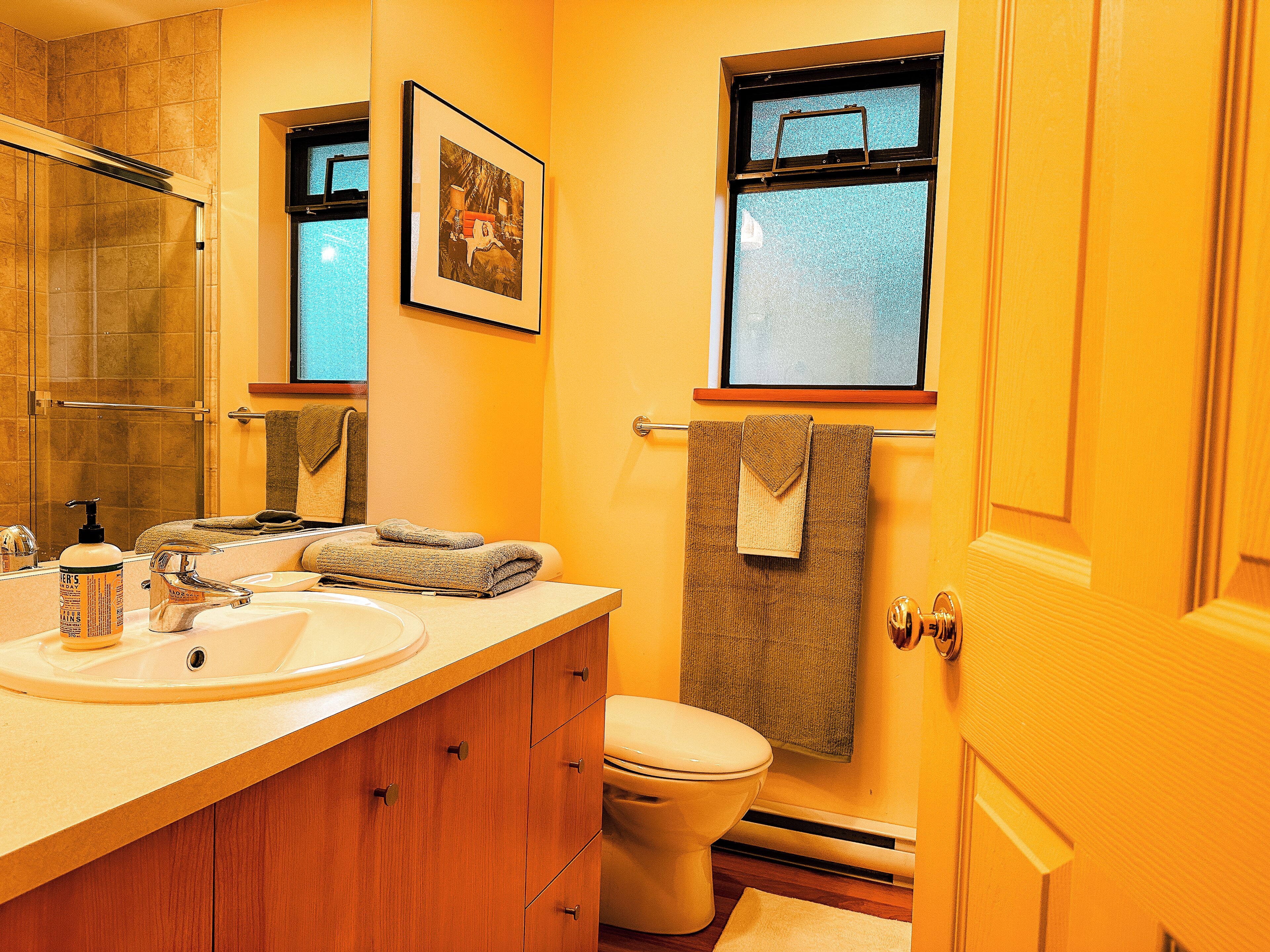 Baño con lavamanos, espejo, toallero, inodoro y ventana con una toalla colgada.